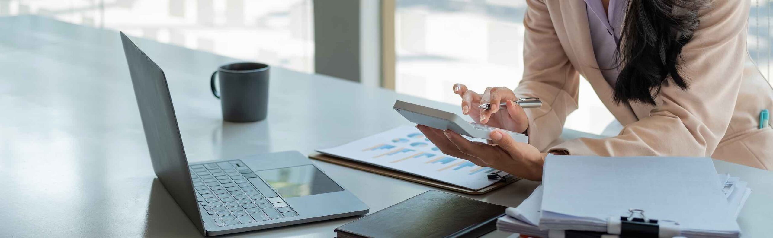 Close up of businesswoman or accountant hand holding pen working on calculator to calculate business data, accountancy document and laptop computer at office, business concept.