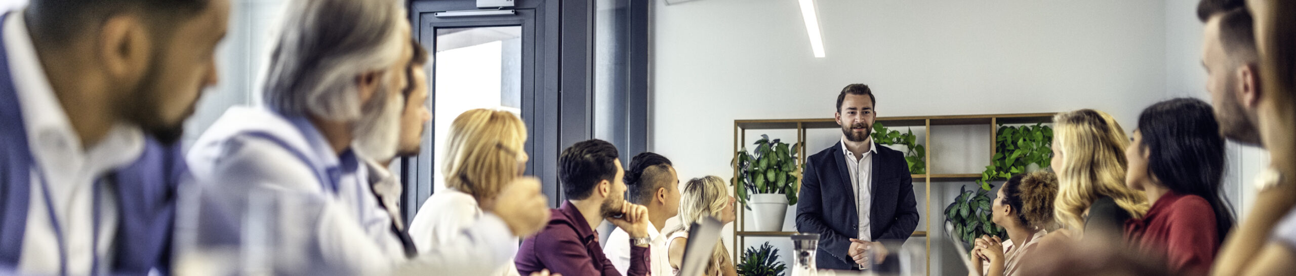 Caucasian manager standing at the end of a conference table talking to people sitting at the table.